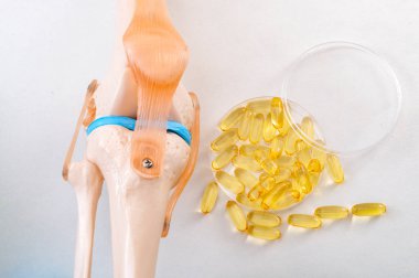 Eklem sağlığı, sağlıklı omega 3 yağ asitleri ve insan dizinin plastik tıp öğretim modeli ve beyaz arka planda izole edilmiş balık yağı hapları ile eklem iltihabı iltihabı konseptini azaltmak