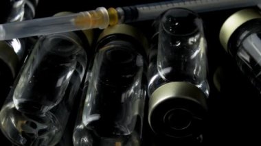 4k panning video of close up on vaccine vials and syringe on dark moody background concept for pandemic vaccination campaign, liquid medicine and disease treatment injection