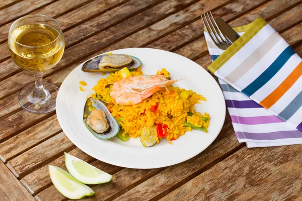 Paella servida en plato sobre mesa de madera —  Fotos de Stock