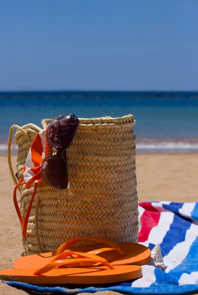 Sunbathing accessories on sandy beach in straw bag — Stock Photo, Image