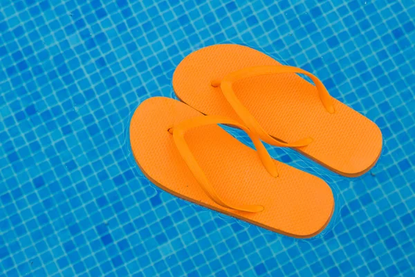 Chanclas naranjas flotando en agua azul de la piscina — Foto de Stock