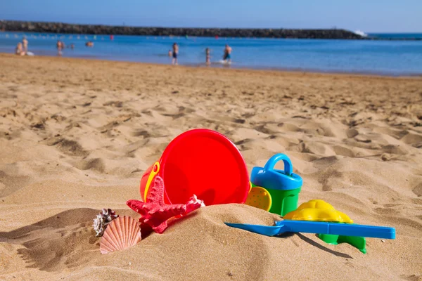 Bucket with plastic beach toys in sand on sea shore — Stock Photo, Image