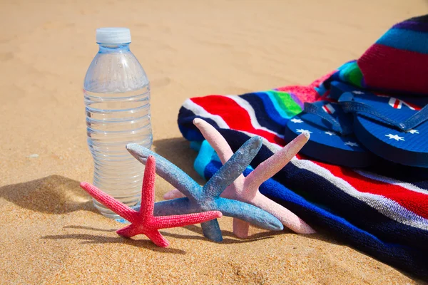 Kum plajındaki su şişe ve plaj havlusu — Stok fotoğraf