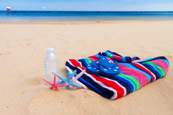 Toalla de playa y botella de agua en la playa de arena — Foto de Stock