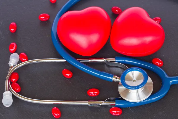 Stéthoscope avec deux coeurs rouges et des pilules — Photo