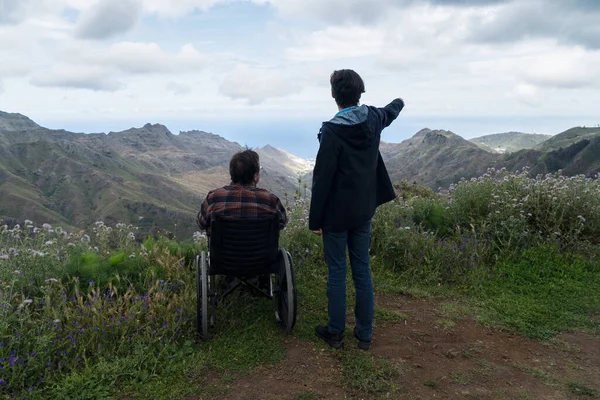 Jeune homme et sa femme en fauteuil roulant voyageant ensemble dans les montagnes — Photo