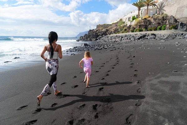 家族のワークアウト 若いスポーティーな母親と小さな娘スポーツ服を一緒に海でビーチで運動し 海岸で実行されます 健康的なライフスタイルのコンセプト — ストック写真