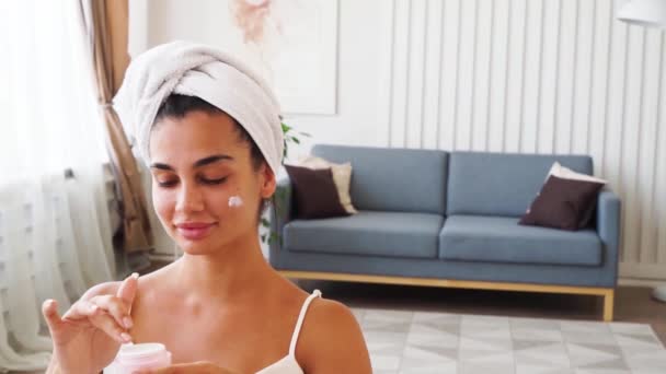 Mulher com toalha embrulhada na cabeça aplicando creme hidratante — Vídeo de Stock