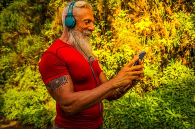 Beyaz sakallı son sınıf öğrencisi dışarıda koşuyor, telefonu tutuyor ve müziği seçiyor.