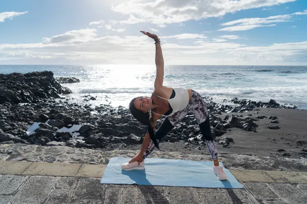 Mulher em roupas esportivas praticando ioga e meditando na praia de manhã — Fotografia de Stock