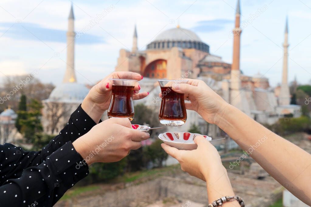 cropped shot of women clinking by coffee glasses in front of mosque in Istanbul, Turkey