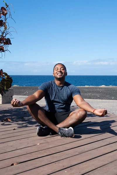 Hombre feliz meditando en posición de loto mientras hace yoga en la playa — Foto de Stock