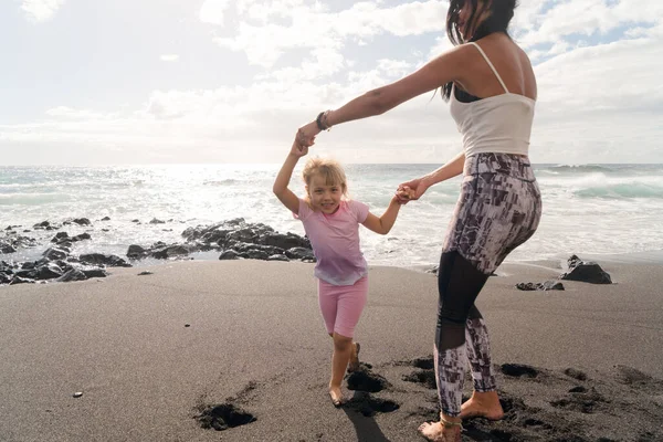 Happy little girl daughter enjoying vacation with mother while standing on beach — Stock Photo, Image