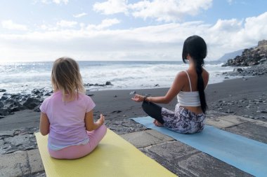Sağlıklı, mutlu bir aile annesi ve kızı deniz kenarında esneme egzersizleri yapıyor.