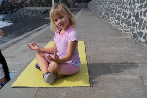 Cute happy little girl in sportswear smiling at camera while while exercising on seaside — Stock Photo, Image