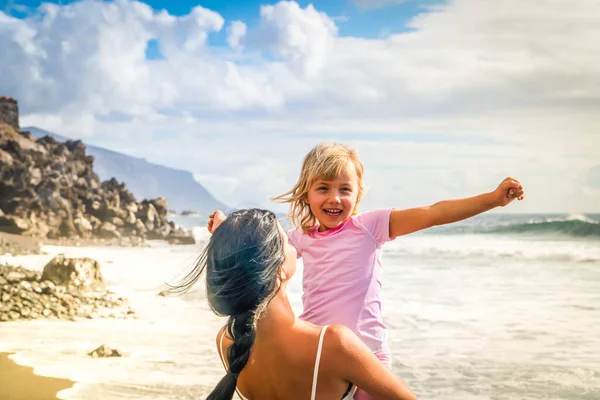 Mutlu küçük kız sahilde dururken annesiyle tatilin tadını çıkarıyor. — Stok fotoğraf