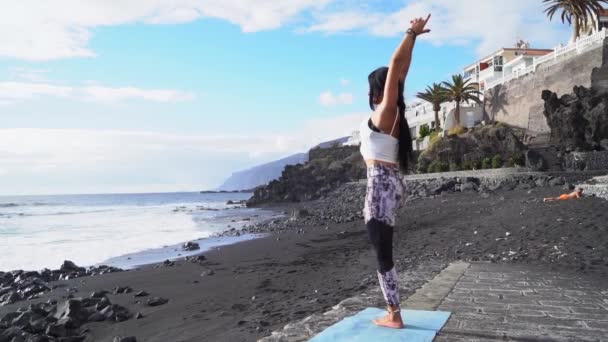 Woman in sport clothes practicing yoga and meditating on beach in morning — Stock Video