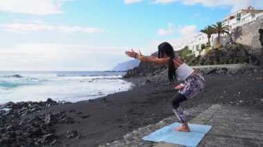 Spor elbiseli kadın sabahları yoga yapıyor ve plajda meditasyon yapıyor.