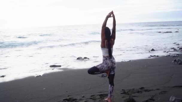 Mulher em roupas esportivas praticando ioga e meditando na praia de manhã — Vídeo de Stock