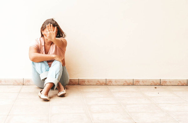 stressful depressed emotional person with anxiety disorder mental health illness sitting feeling bad with back against wall on the floor and showing a reject gesture, toned