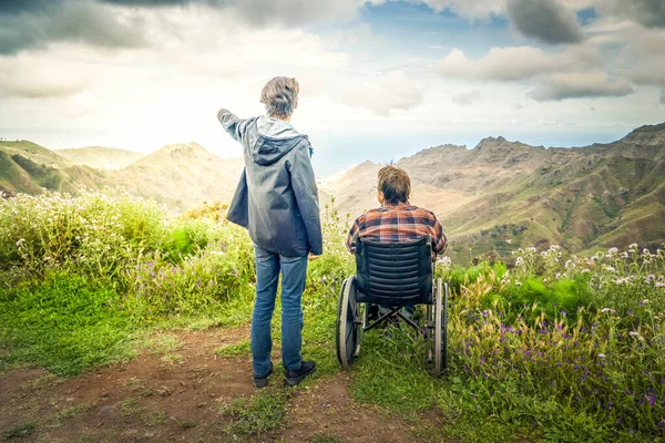 Młody mężczyzna i jego żona na wózku inwalidzkim podróżują razem w górach — Zdjęcie stockowe