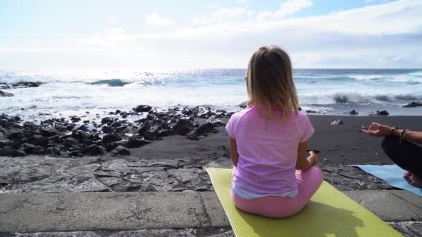 Kleines Mädchen in Sportkleidung praktiziert morgens Yoga und meditiert am Strand — Stockvideo