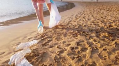 Plajda plastik temizleyen kadın. Gönüllüler çöp torbasında çöp topluyor. Okyanusların plastik kirliliği, sürdürülebilirlik kavramı. Plastik ve temizlik gezegeninden doğanın gönüllü temizliği