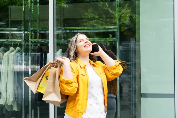 Happy curvy woman with craft ecological bags shopping bags talking on mobile phone enjoying in shopping. Consumerism, shopping, lifestyle concept