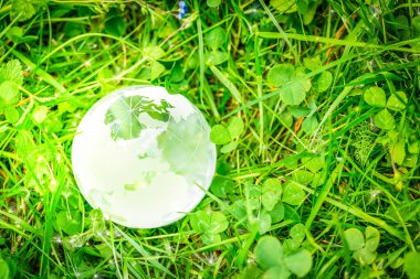 earth protection and sustainable ecology development concept - glass earth planes on green lush background with sunshine
