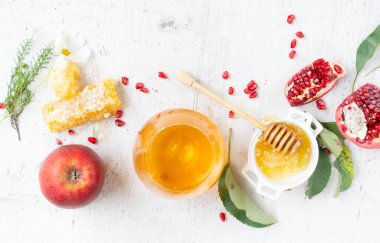 rosh hashana holiday - honey jar with red apple and pomergranate over white desk background. border with copy space