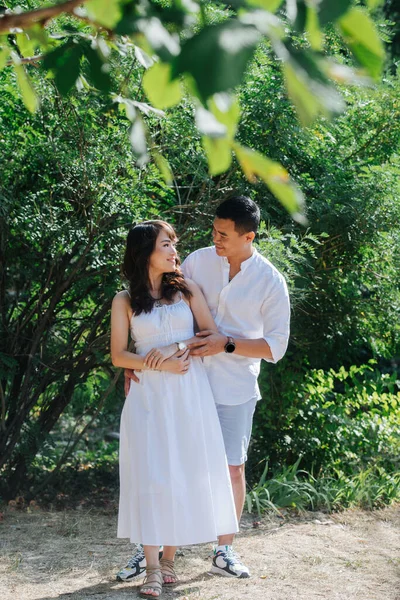 穿着白衣的可爱的亚洲夫妇在公园里消磨时光 男人相互望着对方 从后面抱着女人 他们正享受着初秋最后温暖的日子 — 图库照片