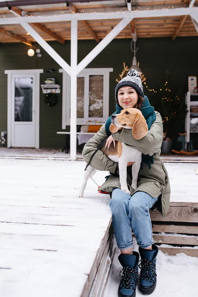 Щаслива Жінка Сидить Сніговій Підлозі Перед Будинком Бігль Собакою Колінах — стокове фото