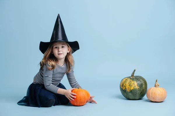 Carina bambina in cappello da strega che gioca con le zucche, seduta sul pavimento. — Foto Stock