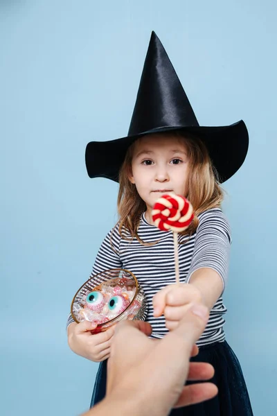 Bambina col cappello da strega che porge un lecca-lecca, facendo gli occhi da cucciolo — Foto Stock