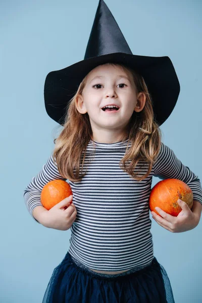 마녀 모자를 쓴 어린 소녀가 작은 호박 두 개를 들고 할로윈 복장을 한 채 — 스톡 사진