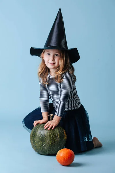 Bella bambina con il cappello da strega che gioca con la zucca verde, appoggiata su di essa — Foto Stock