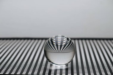 Kare delikli siyah kafes üzerinde mükemmel bir şekilde saydam cam oyuncak küre. Görüntüyü bir lens gibi çarpıtıyor..