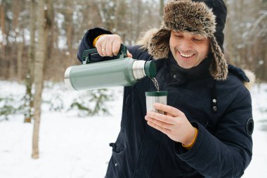 Bir adam kışın ormanda dikilirken termostan sıcak çay döker..