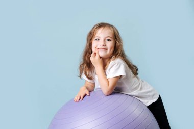 Yanaklarında gamzeleri olan mavi gözlü kıvırcık bebek leylak fitness topuna gülüyor.