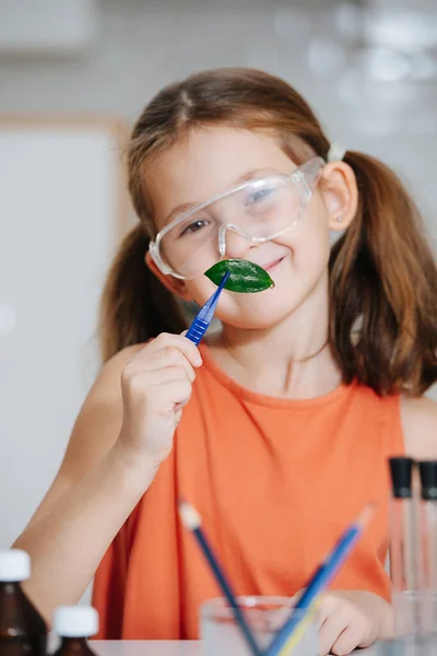 Linda niña sonriente haciendo proyecto de ciencia, sosteniendo una hoja en pinzas — Foto de Stock