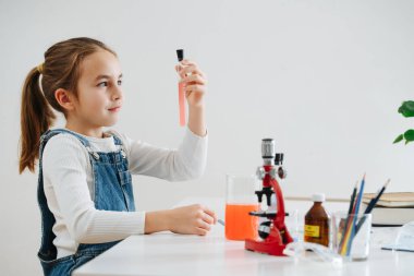 Mermerize kız ev ödevi yapıyor, mataradaki pembe sıvıya bakıyor.