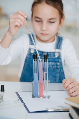 Bulanık kız bilim projesi yapıyor, pipetini şişedeki sıvıyla dolduruyor.