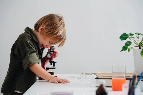 Вид сбоку маленький мальчик делает научный проект, смотрит в микроскоп — стоковое фото