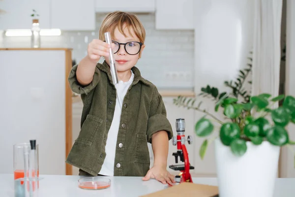 Confident little boy doing science project, showing a flask with clear liquid — 图库照片