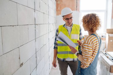 Friendly engineering team discussing the project. Next to a brick wall inside a building under construction.
