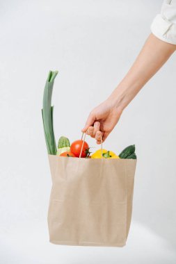 Hand holding grocery paper bag filled with colorful vegetables over white background. Eco friendly compostable products.