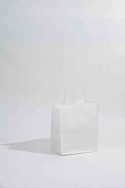 White empty paper bag with rope handles casting a shadow over white background. Eco friendly compostable product.