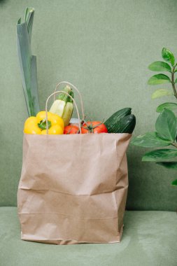 Stuffed paper bag filled with colorful vegetables over green corner. Eco friendly compostable packaging.