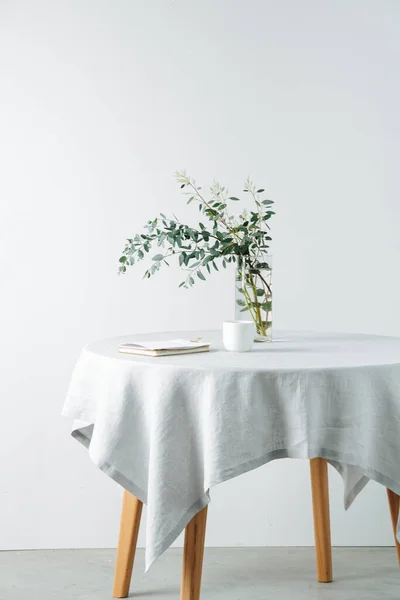 Zijaanzicht ronde tafel met een ruw wit tafelkleed en tak in een pot — Stockfoto