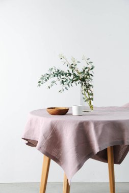 Yuvarlak masa, pürüzlü, pembe bir masa örtüsü ve kavanozda bir dal.